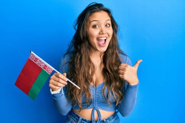 Belarus bayrağını tutan genç İspanyol kız başparmağını yana kaldırmış, ağzı açık gülümsüyor. 