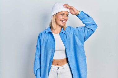 Güzel sarışın kadın, yün şapka takıyor, gülümsüyor, saçlarına dokunuyor, el hareketi yapıyor, çekici ve modaya uygun poz veriyor. 