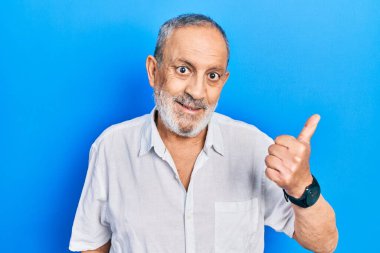 Sakallı, sıradan, beyaz tişörtlü, mutlu yüzlü ve baş parmağıyla yüzünü gösteren yakışıklı bir adam.. 