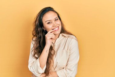 Gündelik kıyafetler giyen genç İspanyol kız kameraya kollarını kavuşturup, elleri çenesinde gülümsüyor. Olumlu düşünmek. 