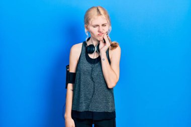 Güzel, beyaz, sarı saçlı, spor kıyafetleri giyen, diş ağrısı ya da diş hastalığından dolayı acı dolu bir ifadeyle dudaklarına dokunan beyaz bir kadın. dişçi 