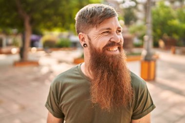 Caddede kendine güvenen genç kızıl saçlı adam gülümsüyor.