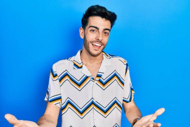 Gündelik kıyafetler giyen genç İspanyol adam güler yüzlü, kolları açık, dostça karşılama, olumlu ve kendinden emin selamlar. 
