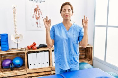 Orta yaşlı İspanyol fizyoterapist kadın ağrı kesici kliniğinde çalışıyor rahatlamış ve parmaklarıyla meditasyon hareketi yaparken gözleri kapalı gülümsüyor. yoga konsepti. 
