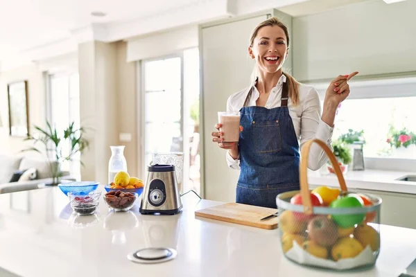 Güzel Sarışın Kadın Önlük Giyip Mutfakta Smoothie Içerken Gülümsüyor — Stok fotoğraf