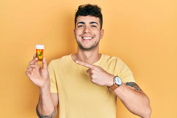 Молодий Іспаномовний Чоловік Тримає Таблетки Посміхаючись Щасливим Вказуючи Рукою Пальцем — стокове фото
