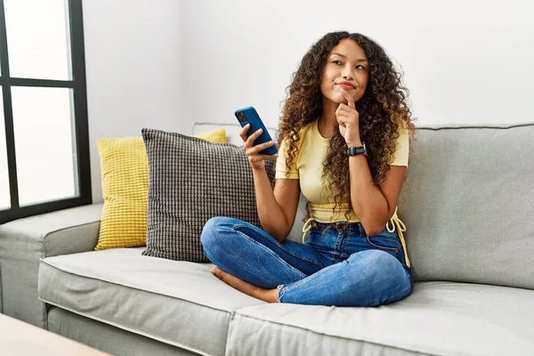 Beautiful Hispanic Woman Sitting Sofa Home Using Smartphone Hand Chin — Stockfoto