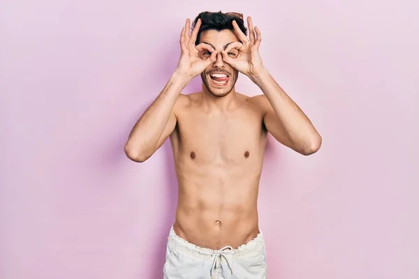 Young Hispanic Man Wearing Swimwear Shirtless Doing Gesture Binoculars Sticking — Stock Photo, Image