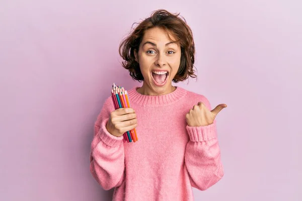 Joven Morena Sosteniendo Lápices Colores Apuntando Con Pulgar Hacia Lado — Foto de Stock