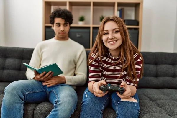Vrouw Spelen Video Game Terwijl Ongelukkige Vriend Boek Lezen Thuis — Stockfoto
