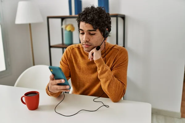 若いヒスパニック系の男は自宅でテーブルの上に座っているスマートフォンを使用してビデオ通話を持っています — ストック写真