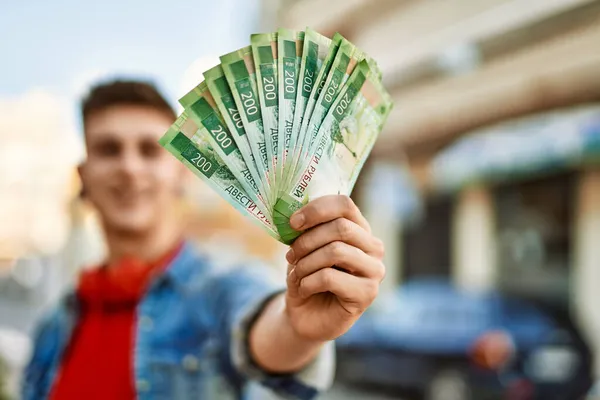 Young caucasian guy smiling holding russian ruble banknotes at the city