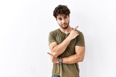 Hispanic man standing over isolated white background pointing with hand finger to the side showing advertisement, serious and calm face 