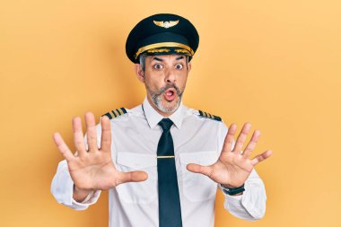 Handsome middle age man with grey hair wearing airplane pilot uniform doing stop gesture with hands palms, angry and frustration expression 
