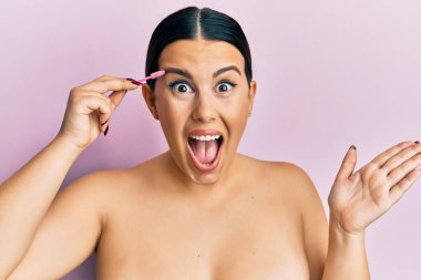 Güzel esmer kadın kaşlarını fırçayla fırçalıyor zaferi mutlu bir gülümsemeyle kutluyor ve kazanan el kaldırarak ifade ediyor. 