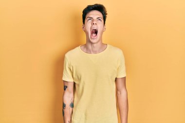 Gündelik sarı tişört giyen genç İspanyol adam kızgın ve kızgın bağırıyor öfkeyle bağırıyor. öfke ve agresif konsept. 