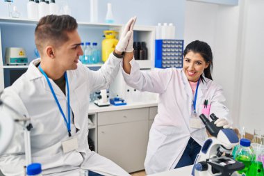 Erkek ve kadın bilim adamları laboratuarda elleri havada beşlik çakıyor.