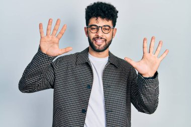 Young arab man with beard wearing glasses showing and pointing up with fingers number ten while smiling confident and happy. 