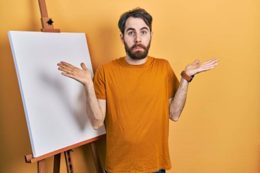 Boyacı sehpasının yanında duran beyaz sakallı adam hiçbir şeyden habersiz ve kolları açık, hiçbir fikri ve şüpheli bir yüzü var.. 