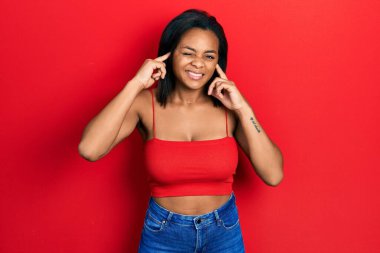 Gürültülü müzik sesi için kolsuz tişörtle kulakları parmaklarla kapatan Afro-Amerikalı genç bir kız. sağır kavramı. 