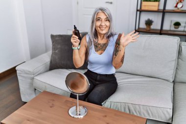 Gece serumu kullanan orta yaşlı, kır saçlı bir kadın koltukta oturmuş başarıyı mutlu bir gülümsemeyle kutluyor ve kazanan el kaldırarak ifade ediyor. 