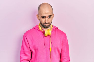 Spor kıyafetleri giyen, kulaklık takan kuşkucu ve sinirli genç bir adam sorun yüzünden surat asıyor. negatif kişi. 