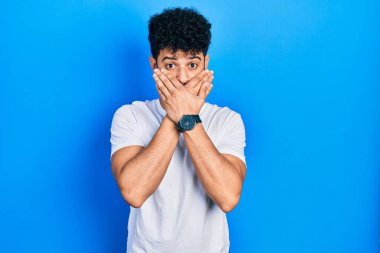 Young arab man with beard wearing casual white t shirt shocked covering mouth with hands for mistake. secret concept. 