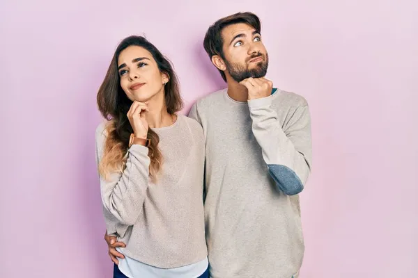 若いヒスパニック系のカップルの質問については 集中的な表現を考えて顎に手でカジュアルな服を着て 思慮深い顔で笑顔 疑わしい概念 — ストック写真