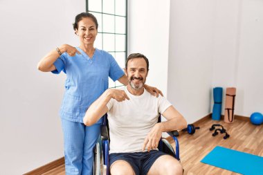 Tekerlekli sandalyede oturan İspanyol orta yaşlı bir adam ve rehabilitasyon kliniğindeki hemşire mutlu ve gururlu bir kendini işaret ediyor. 