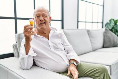 Elinde haplar olan yaşlı bir adam kameraya seksi bir ifadeyle bakıyor, neşeli ve mutlu bir yüz.. 