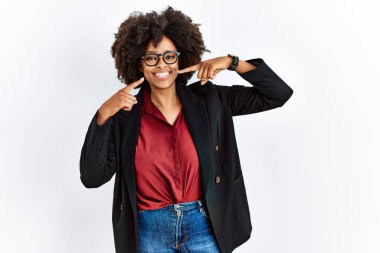 Afro saçlı, iş ceketi giyen ve gözlüklü neşeli gülümseyen, parmakları ve ağzıyla işaret eden Afro-Amerikalı kadın. diş sağlığı kavramı. 