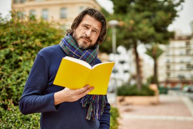 Orta yaşlı yakışıklı bir adam parkta kitap okuyor.