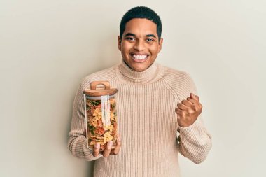 Genç, yakışıklı İspanyol adam elinde makarna kavanozuyla gururla bağırıyor zaferi ve başarıyı kutluyor. 