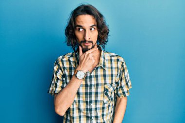 Elleri çenesinde gündelik giysiler içinde soru soran genç İspanyol bir adam, düşünceli bir ifade. Düşünceli bir yüzle gülümsüyor. şüphe kavramı. 