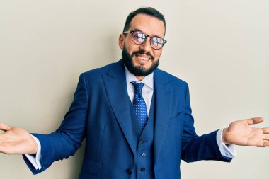 Sakallı, takım elbiseli, kravatlı, elleri ve kolları havada, kafası karışmış genç bir adam. şüphe kavramı. 