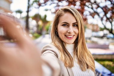 Gülümseyen genç sarışın kadın caddedeki akıllı telefonun yanında özçekim yapıyor.