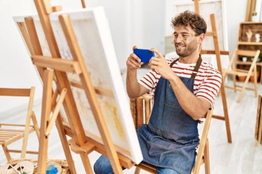 Young hispanic man make photo to draw using smartphone at art studio