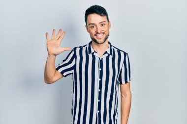 Gündelik kıyafetler giyen genç İspanyol adam beş numarayı gösterip işaret ederken kendinden emin ve mutlu bir şekilde gülümsüyor.. 