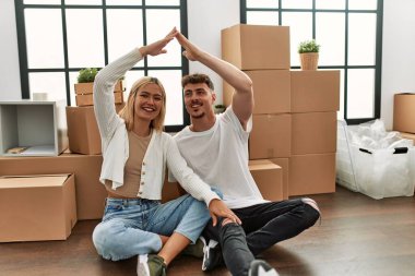 Genç beyaz çift gülümseyerek yeni evlerinde ev sembolü yapıyor..