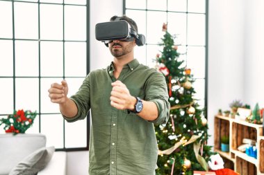 VR gözlük takan genç İspanyol adam Noel ağacının yanında duruyor.