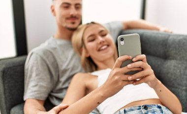 Genç beyaz çift evde akıllı telefon kullanarak mutlu bir şekilde gülümsüyor..