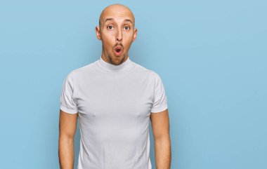 Bald man with beard wearing casual white t shirt afraid and shocked with surprise expression, fear and excited face. 