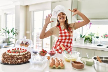 Güzel, genç, esmer pasta şefi kadın mutfakta hamur işleri pişiriyor ve yedinci parmaklarını gösterip işaret ederken kendinden emin ve mutlu gülümsüyor.. 