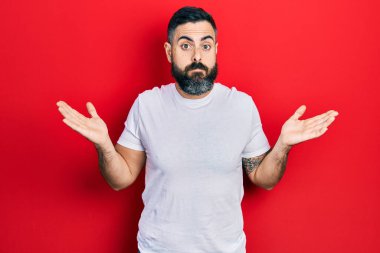 Gündelik beyaz tişört giyen genç İspanyol adam habersiz ve kolları açık, hiçbir fikrim yok ve şüpheli bir yüzüm var.. 