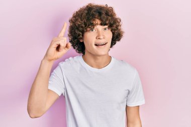 Handsome young man wearing casual white t shirt pointing finger up with successful idea. exited and happy. number one. 