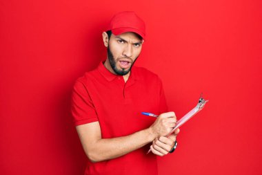 Sakallı, kurye üniformalı İspanyol bir adam. Şok olmuş suratıyla pano tutuyor. Şüpheci ve alaycı görünüyor. 