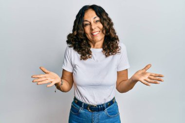 Orta yaşlı İspanyol kadın gündelik beyaz tişört giyiyor. Hiçbir şeyden habersiz ve elleri ve kolları havada kafası karışmış bir ifade. şüphe kavramı. 