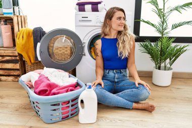 Çamaşır sepetinin yanında oturan genç ve güzel bir kadın. Gülümsüyor, yan tarafa bakıyor ve düşünüyor.. 