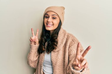 Yün kazak ve kış şapkası giyen genç İspanyol kadın kameraya bakıp zafer işareti yapıyor. İki numara.. 