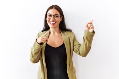 Genç esmer kadın izole edilmiş arka planda duruyor gülümsüyor ve kameraya bakıyor iki eliyle ve parmaklarıyla kenarı işaret ediyor.. 
